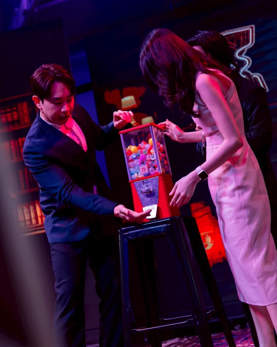 Patrick Kun on stage with two spectators reaching into The Machine under red and purple light
