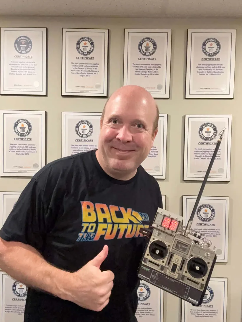 Ian Stewart holding The Remote in front of a wall of his Guinness World Records certificates